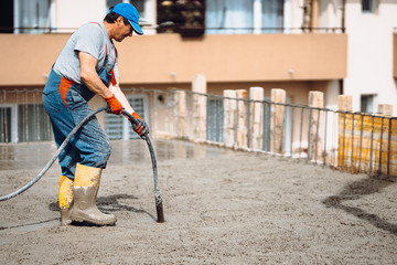 Caucasian worker using a concrete vibrator at the construction site during cement pouring - obrazy, fototapety, plakaty