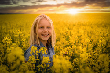 Ein lachendes Kind mit einer Rapspflanze in der Hand und ein gelbes Rapsfeld im Sonnenuntergang