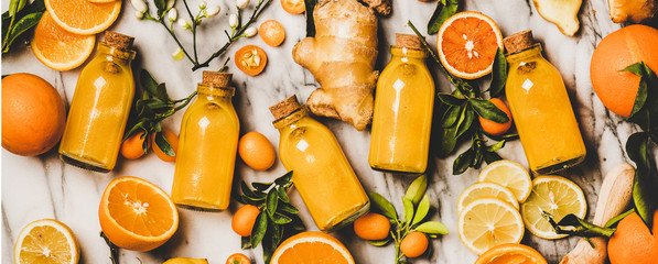 Immune boosting vitamin health defending drink. Flat-lay of fresh turmeric, ginger, citrus juice shot in bottles over marble background, top view, wide composition. Vegan Immunity system booster