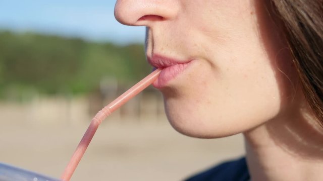Slow motion young girl wearing sunglasses, sipping a chocolate cocktail with a straw. Drink outdoors on a summer day