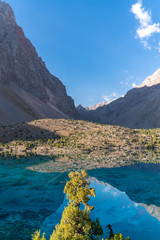 Obraz premium The beautiful mountain trekking road with clear blue sky and rocky hills and the view of Alaudin lake in Fann mountains in Tajikistan