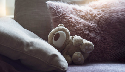 Dramatic photo of Teddy bear is lying on sofa in dark room with sunlight shining from window, lowkey light shot of Lonely teddy laying down alone in living room international missing children's day