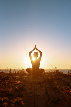 Silhouette meditation girl on the background of the stunning sea and sunset. Yoga, fitness and healthy lifestyle. Woman doing meditation in the beach. Vertical stock photo