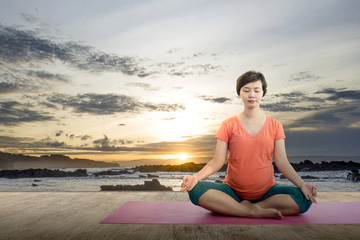 Fototapeta na wymiar Asian pregnant woman is practicing yoga in yoga mat