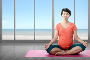 Asian pregnant woman is practicing yoga in a yoga mat at home