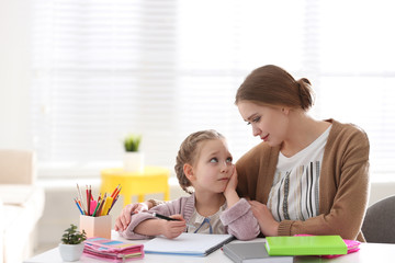 Woman helping her daughter with homework at table indoors