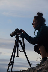A woman taking photos in the mountains at sunset with a professional photo camera