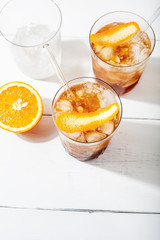 Refreshing soft drinks, including a cold drink coffee cocktail and citrus espresso tonic, decorated with orange zest and glass straws on white background