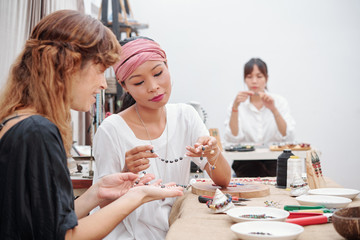 Smiling teacher looking at beautiful stone necklace her student made during lesson