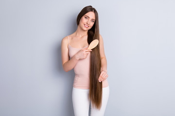 Photo of peaceful attractive cheerful model lady long hairdo hold favorite wooden comb carefully brushing strong curls wear beige singlet trousers isolated grey color background