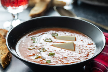 Rustic tomato soup with white cheese in black bowl