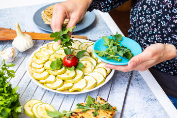 Woman add green  rucola to baked, roasted, grill zucchini round slices. Vegetables vegan healthy food