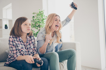 Obraz premium Photo of crazy funny blond lady yelling mom daughter sit sofa hold joystick play video game winner loser stay home quarantine spend weekend together best friends living room indoors