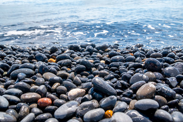 Smooth, round and wet black pebbles next to the water at the volcanic beach in Chios island, Greece. Natural background with copy space