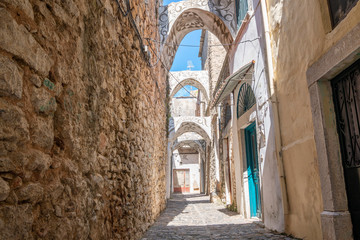A narrow alley with stone wall and houses with traditional geometric patterns on the facades and building arch. No people. An old motorbike standing in a doorway