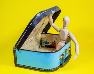 The lid of an old suitcase is held open by a wooden doll. Suitcase is packed for the next holiday