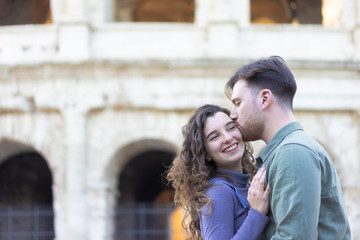Naklejka premium Happy couple of travelers having fun, cute couple kissing on a sunny day near of Coliseum. Happy tourists visiting famous monuments. Honeymoon trip, tourism, love vacation and vacation trip concept 