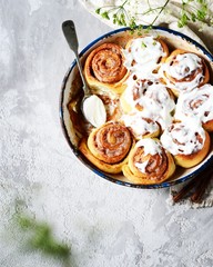 Cinnamon buns in a baking dish with cream cheese curd on a gray background