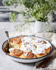 Cinnamon buns in a baking dish with cream cheese curd on a gray background