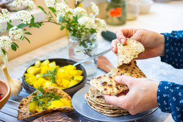 Woman tear indian chapati bread or tortilla flatbreads with herbs and vegetables. Vegan food.
