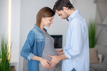 Young dark-haired man touching his wifes pregnant abdomen