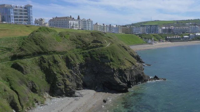 Revealing shot of Port Erin coastal town and beach area.  Sea crashing into cliffs