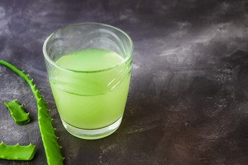 Aloe vera juice with fresh leaves on a grey background