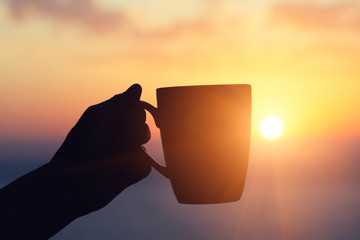 young woman's hand holding coffee cup and drinking morning coffee at sunrise outside
