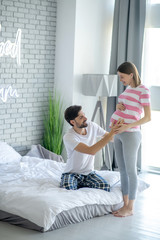Bearded man touching his pregnant wifes abdomen and feeling thrilled