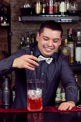 A young guy working as a bartender behind a bar is preparing drinks for customers.