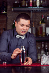 A young guy working as a bartender behind a bar is preparing drinks for customers.