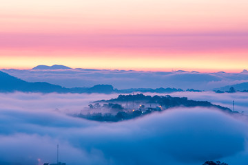 Obraz premium Mountains in fog at beautiful night in autumn in Dalat city, Vietnam. Landscape with Langbiang mountain valley, low clouds, forest, colorful sky with stars, city illumination at dusk.