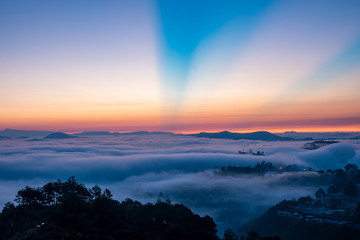 Fototapeta na wymiar Mountains in fog at beautiful morning in autumn. Landscape with Langbiang mountain valley, low clouds, forest, colorful sky , city illumination at dusk.