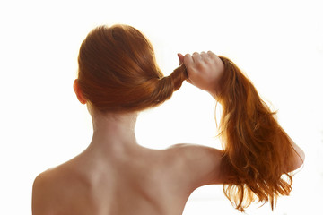 girl stands with her back and holds red hair in her hand