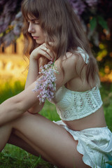 summer portrait of beautiful girl sitting on the grass and holding lilac branch