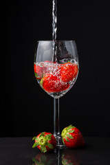 Close-up of glass cup with strawberries, with water falling, two strawberries, on slate, black background, vertical