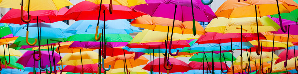 A place in the center of Paris with colorful umbrellas instead of ceiling. Yellow red pink blue green orange. Sunlight coming from the top. Wind is blowing. Banner © ArtSys