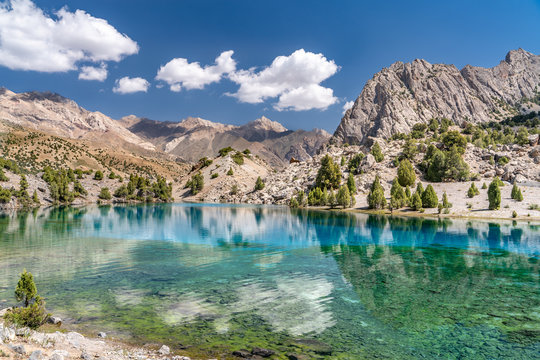 The beautiful mountain trekking road with clear blue sky and rocky hills and the view of Alaudin lake in Fann mountains in Tajikistan