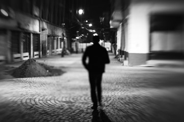 Street abstract using a lensbaby with a man silhouette walking on an empty street late evening.