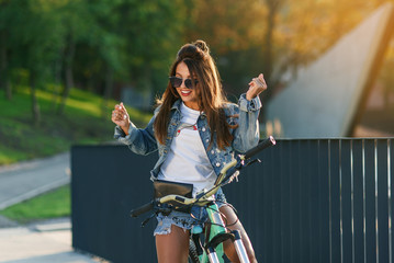 Attractive tempting young girl in fashion jeans clothes wears stylish glasses ,sitting on the bicycle and posing on camera at summer evening. Slow motion