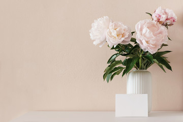 Spring, summer floral still life. Pink peony flowers bouquet in porcelain vase on white wooden table. Blank greeting card mockup scene. Nude wall backround. Empty copy psace, no people, front view.