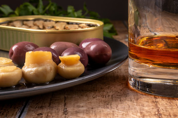 Whiskey in a glass and an appetizer for alcohol: pickled champignons, olives, sprats. Snack for whiskey, cognac, brandy.