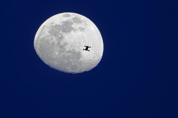View of a drone flying in front of the moon and its craters over a blue night sky