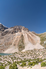 The beautiful mountain trekking road with clear blue sky and rocky hills and fresh mountain lake in Fann mountains in Tajikistan