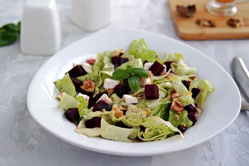 Green salad with boiled beetroot, feta and walnuts in a white plate on a gray concrete background. Seasoned with olive oil, grain mustard and vinegar. Healthy food.