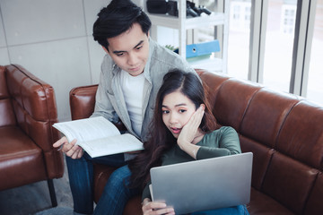 Couple Love Having Enjoy Relaxation on Sofa at Their Home, Attractive Asian Couple Happiness in Romantic Moments at Living Room While Reading Magazine and Work at Home. Relaxing and Lifestyles Concept