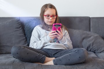 Bored child sitting on the couch and holding a mobile phone.Stay at home. Teenage girl bored...