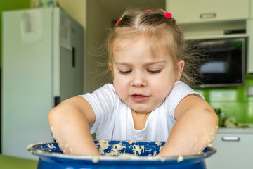 little girl 3-4 years old plays with the dough in a large blue pan in the kitchen. activities with children on self-isolation