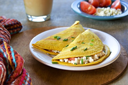 Chilla, tortillas or pancakes made from chickpea flour stuffed with cheese panir and tomato on a white plate on a gray concrete background. Indian food, street food. Vegetarian recipes.