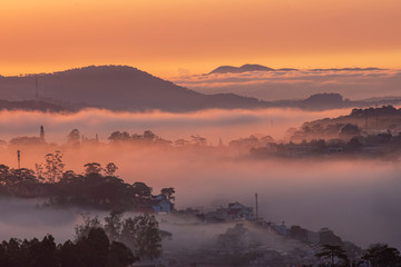Mountains in fog at beautiful morning in autumn in Dalat city, Vietnam. Landscape with Langbiang mountain valley, low clouds, forest, colorful sky , city illumination at dusk.